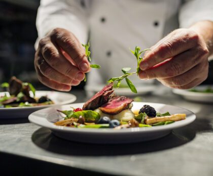 Chef adding the final flourish by adding some liquorice flavoured  parsley to the dish. The dish is, pan fried pink duck breast onto a bed of parsnip puree with seasonal autumn vegetables and berries. Colour, horizontal with some copy space, photographed on location in a restaurant on the island of Møn in Denmark.